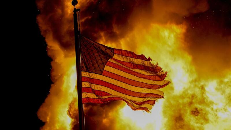 A flag flies over a department of corrections building ablaze during protests, late Monday,...